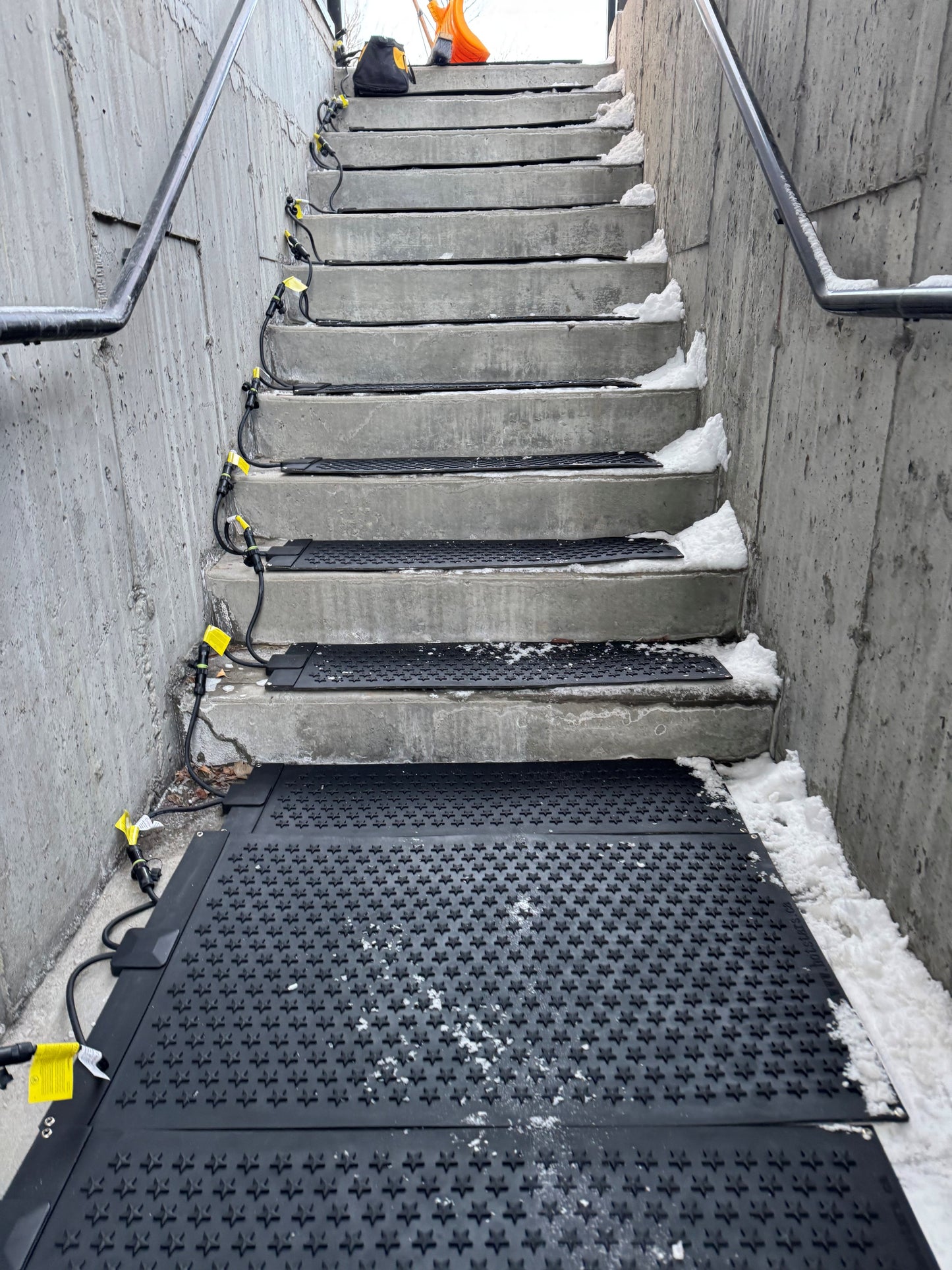 Ice melting products like HOTStars™ Stair Treads shown on outdoor stairs with partial snow removal. Durable heated mats for safe winter walkways.